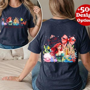 Puede incluir: Camiseta azul marino con una colorida ilustraci&oacute;n de una sirena, un castillo y criaturas marinas. La parte delantera de la camiseta tiene el texto "Ariel's Adventures". La parte trasera de la camiseta tiene el texto "The Little Mermaid".