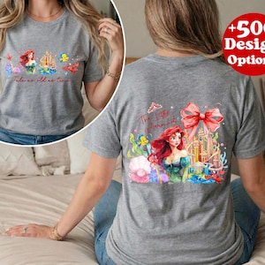 Puede incluir: Camiseta gris con una colorida ilustraci&oacute;n de Ariel de La Sirenita. La parte delantera de la camiseta tiene a Ariel y otros personajes con el texto "Tale as old as time". La parte trasera tiene un dise&ntilde;o m&aacute;s grande con Ariel, un castillo y un gran lazo.