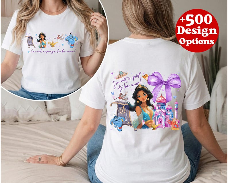 Puede incluir: Camiseta blanca con una colorida ilustraci&oacute;n de una princesa, una alfombra m&aacute;gica, un genio y un palacio. Tambi&eacute;n se muestra el texto "I'm not a prize to be won!". La camiseta tiene cuello redondo y mangas cortas.