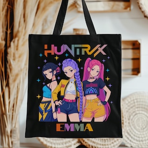 May include: Black tote bag featuring a colorful graphic of three anime-style women. The bag has the text "HUNTRAX" and "EMMA" in a rainbow gradient. The women are in various outfits, with colorful hair and star accents.