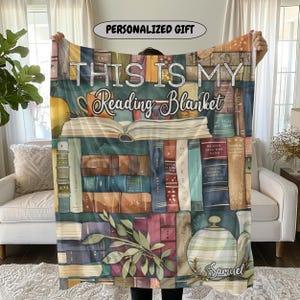 May include: A personalized reading blanket featuring a watercolor design of a bookshelf filled with books, a teacup, and a teapot. The blanket has the text "THIS IS MY Reading Blanket" and the name "Samuel".