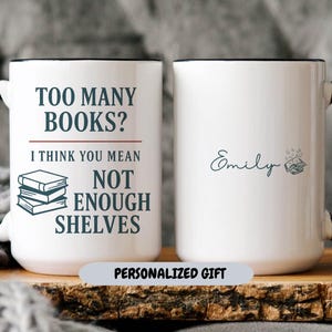 May include: White ceramic mug with a black handle and rim. The mug features the text "TOO MANY BOOKS? I THINK YOU MEAN NOT ENOUGH SHELVES" and a stack of books. The other side is personalized with the name "Emily".
