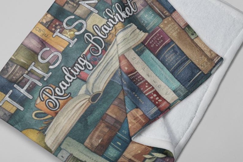May include: A cozy reading blanket featuring a design of stacked books in various colors. The blanket has the text "THIS IS MY Reading Blanket" in a decorative font. The blanket is folded over, revealing a white, soft underside.