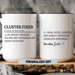 May include: Two white mugs with black rims and handles. The mug on the left has the text "CLUSTER FIXER /KLASTƏR WISPƏRƏR/ (NOUN) 1. AN EXPERT PROBLEM SOLVER WHO UNTANGLES ANY GIVEN SITUATION". The mug on the right has the text "2. CALM, LEVEL-HEADED, AND ALMOST GENIUS IN HANDLING NONSENSE. See also: John".