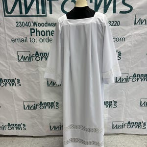 May include: White liturgical cassock with lace trim. The cassock is a long, flowing garment worn by clergy.