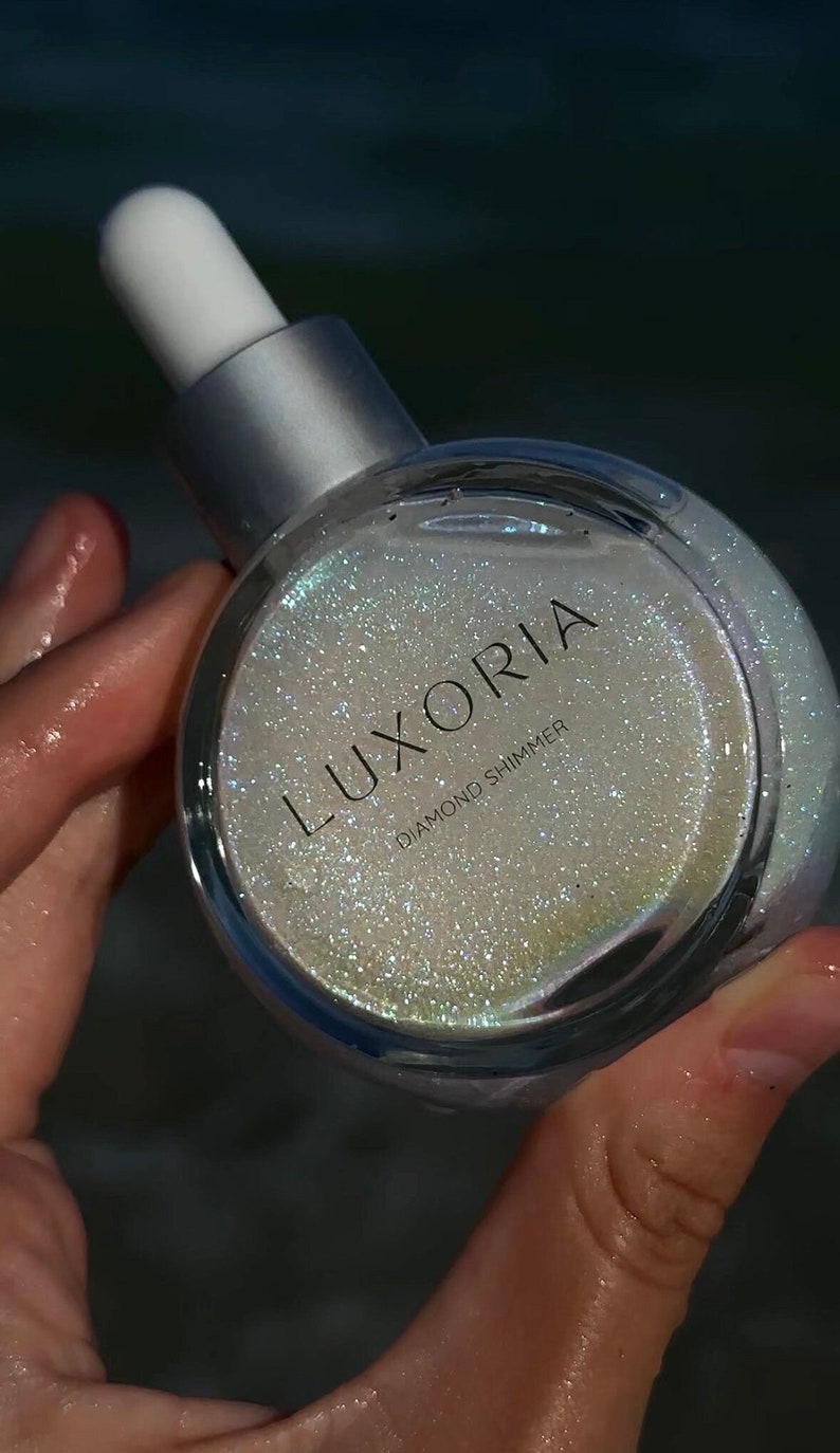 May include: A clear glass bottle with a silver cap and a white dropper. The bottle contains a shimmering, iridescent liquid with the text "LUXORIA DIAMOND SHIMMER" on the label.