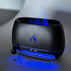 May include: A black essential oil diffuser with a blue light and a small bottle of oil. The diffuser has a button labelled "Light" and a button labelled "Mist".