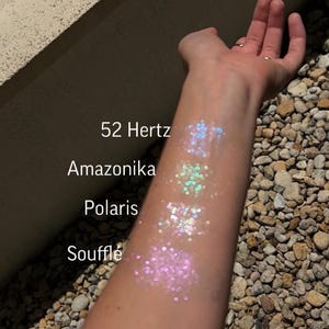 May include: A person's arm with four swatches of iridescent glitter on it. The swatches are labeled "Souffle", "Polaris", "Amazonika", and "52 Hertz".