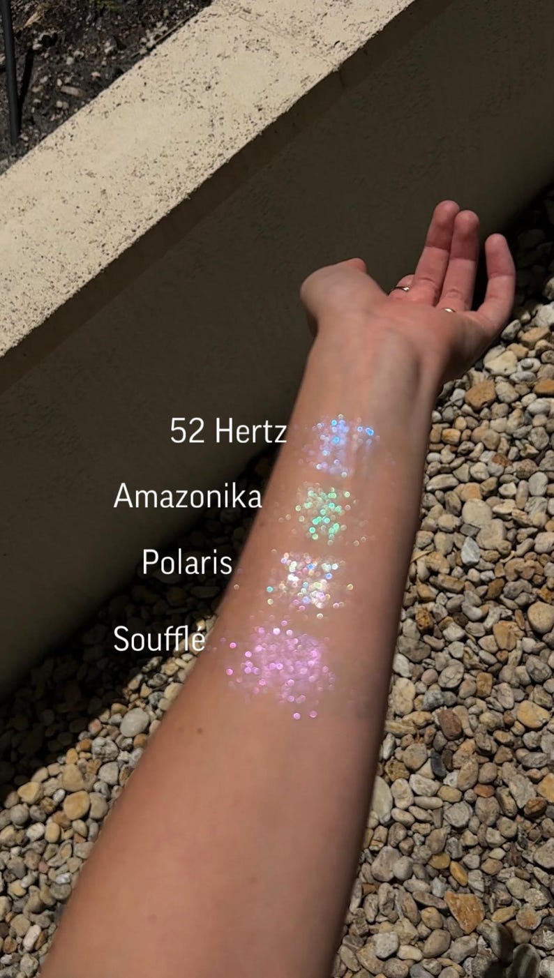 May include: A person's arm with four swatches of iridescent glitter on it. The swatches are labeled "Souffle", "Polaris", "Amazonika", and "52 Hertz".