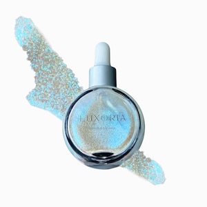 May include: A clear glass bottle with a silver cap and dropper. The bottle contains a shimmering, iridescent liquid. The label on the bottle reads "LUXORIA DIAMOND SHIMMER".
