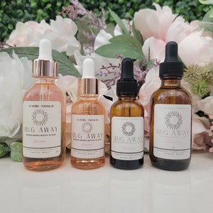 May include: Four amber glass bottles with white labels and black caps. The labels read "Bug Away" and "Lavender". The bottles are on a white surface.