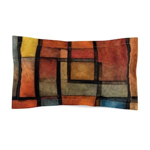 Pode incluir: Uma almofada decorativa com um padrão geométrico de quadrados e retângulos em tons de laranja, vermelho, castanho, amarelo, azul e cinza.