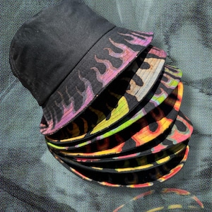 May include: A stack of black bucket hats with a flame design on the brim. The flames are in shades of pink, yellow, and orange. The hats are made of a soft material.