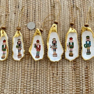 May include: Eight gold-painted oyster shell ornaments with painted nutcracker designs. Each ornament features a different nutcracker with a unique costume and accessories.