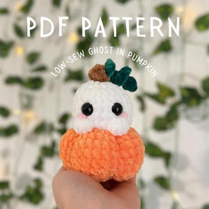 May include: A crocheted ghost in a pumpkin costume. The ghost is white with black eyes and a brown stem on top. The pumpkin is orange and has a green leaf.
