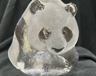 May include: A clear glass sculpture of a panda bear sitting with its paws tucked in. The panda has black eyes, ears, and markings around its eyes.