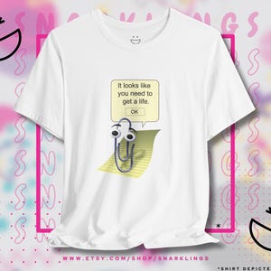 May include: White t-shirt with a graphic of a paperclip with eyes and a speech bubble that says "It looks like you need to get a life. OK."