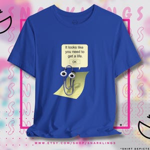 May include: A royal blue t-shirt with a white paperclip with googly eyes on a yellow piece of lined paper. The paperclip is walking across the paper. The text on the shirt reads "It looks like you need to get a life. OK."