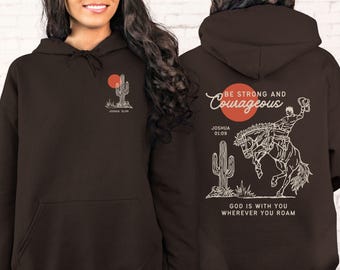 Könnte beinhalten: Ein dunkelbrauner Kapuzenpullover mit Design auf Vorder- und Rückseite. Die Vorderseite zeigt eine Kaktus- und Sonnengrafik mit Text. Die Rückseite zeigt einen Cowboy auf einem Pferd, Kaktus und Text "Be Strong and Courageous."