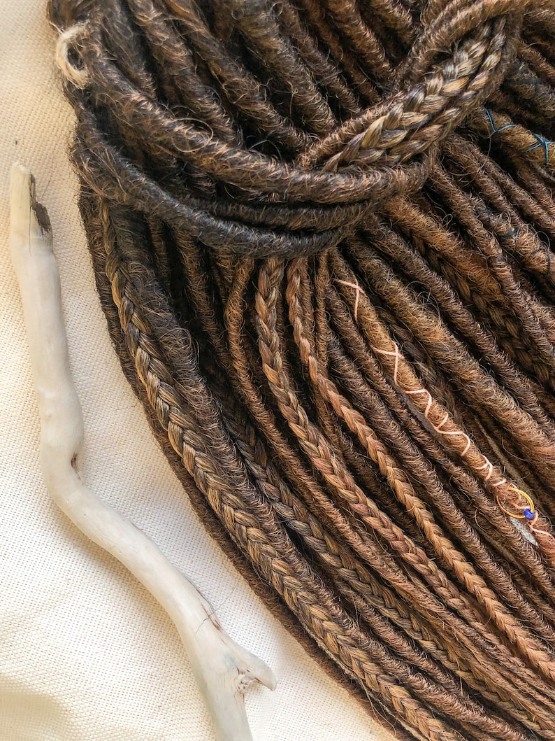 May include: A bundle of brown and blonde synthetic dreadlocks. The dreadlocks are arranged in a loose pile and have a natural, textured appearance.
