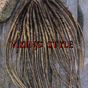 May include: A set of brown and blonde synthetic dreadlocks with red and black accents. The dreadlocks are arranged in a straight line and have a "VIKING STYLE" label.