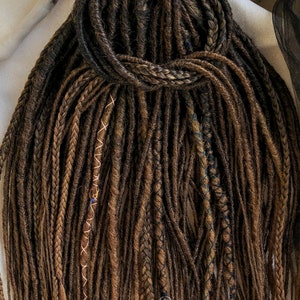 May include: A set of brown synthetic dreadlocks with various colored accents, including blue, gold, and copper. The dreadlocks are tied together at the top.