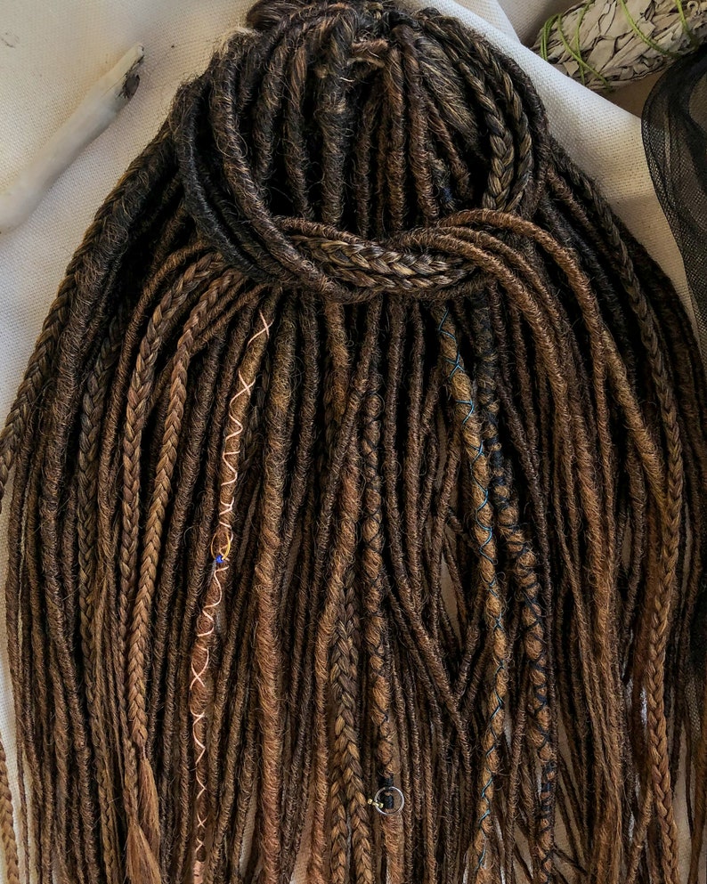 May include: A set of brown synthetic dreadlocks with various colored accents, including blue, gold, and copper. The dreadlocks are tied together at the top.