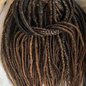 May include: A set of brown synthetic dreadlocks with gold and blue accents. The dreadlocks are long and straight, and they are arranged in a loose, flowing style.