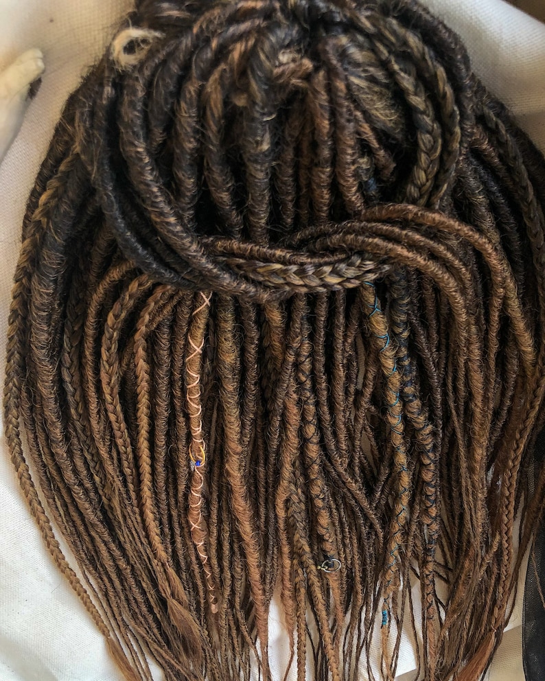 May include: A set of brown synthetic dreadlocks with gold and blue accents. The dreadlocks are long and straight, and they are arranged in a loose, flowing style.
