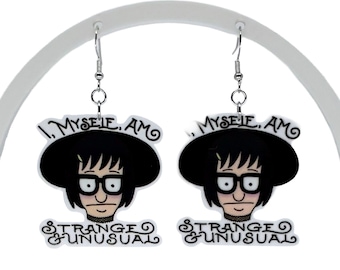 May include: A pair of dangle earrings featuring a cartoon character with black hair, glasses, and a wide-brimmed hat. The text "I, MYSELF, AM STRANGE & UNUSUAL" is printed in black lettering above and below the character's face on a white background.
