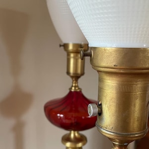 May include: Two vintage table lamps with red glass bases and white frosted glass shades. The lamps have brass accents and a rotary switch on the base.