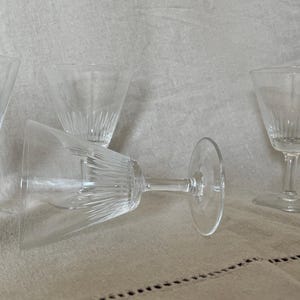 May include: Four clear, stemmed cocktail glasses with a textured, vertical-line design. One glass is lying on its side. The glasses are on a neutral-colored, textured surface.