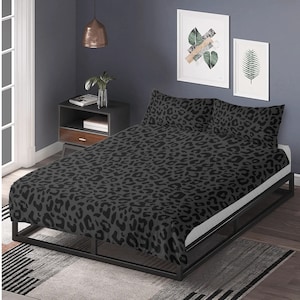 May include: A bed with a black metal frame and a gray and black leopard print duvet cover and pillowcases. The bed is in a room with a dark gray wall, a side table, and framed artwork.