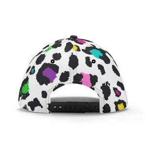 Pode incluir: Um bon&eacute; de beisebol branco com um padr&atilde;o de estampa de leopardo preto e branco. A estampa apresenta detalhes coloridos em rosa, verde, azul, roxo e amarelo.