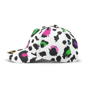 Pode incluir: Um bon&eacute; de beisebol branco com um padr&atilde;o de estampa de leopardo preto e branco. A estampa apresenta manchas coloridas em rosa, verde, amarelo e roxo.