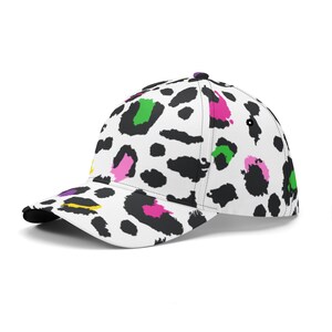 Pode incluir: Um bon&eacute; de beisebol branco com um padr&atilde;o de estampa de leopardo preto e branco. A estampa apresenta detalhes coloridos em rosa, verde e amarelo.