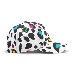 Pode incluir: Um bon&eacute; de beisebol branco com um padr&atilde;o de estampa de leopardo preto e branco. A estampa tem respingos de rosa, amarelo, verde e azul.