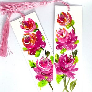 May include: Two pink floral bookmarks with green leaves and a pink tassel.