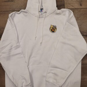 May include: White hooded sweatshirt with a kangaroo pocket and drawstring. Features a small, colourful embroidered patch on the chest. The patch depicts a cartoon character with the text "This is Fine".