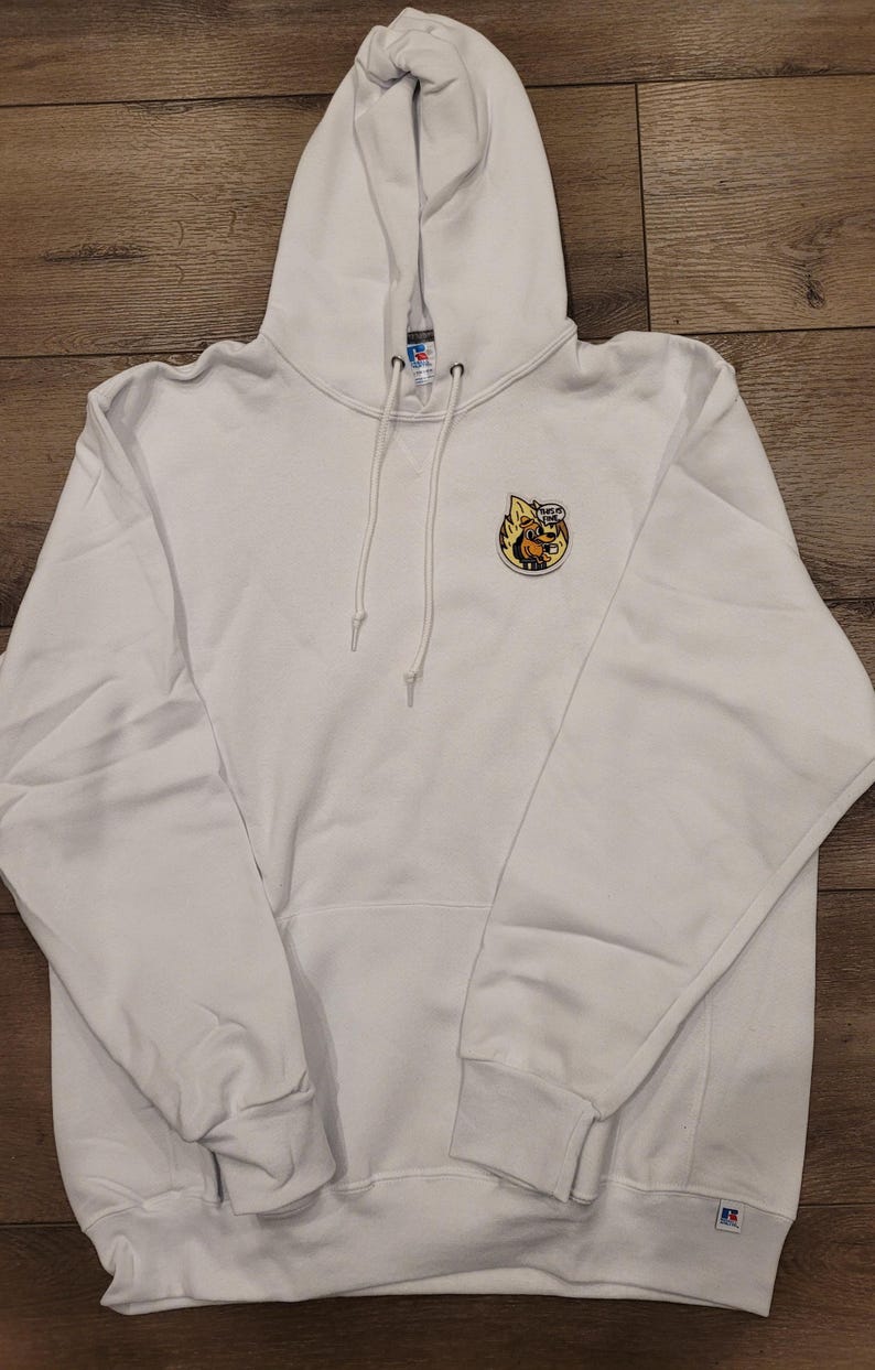 May include: White hooded sweatshirt with a kangaroo pocket and drawstring. Features a small, colourful embroidered patch on the chest. The patch depicts a cartoon character with the text "This is Fine".