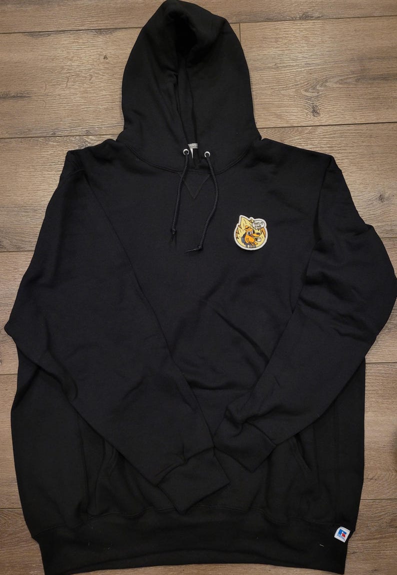 May include: Black hooded sweatshirt with a drawstring and a small patch featuring a cartoon dog on fire. The sweatshirt has a kangaroo pocket and a Russell Athletic logo on the lower left.