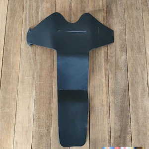 May include: A black leatherette item, possibly a garment accessory or craft supply, lies on a wooden surface. The item has a unique shape with a wide top and a long, narrow extension. The material appears smooth and has a matte finish.