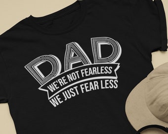 Peut inclure: T-shirt noir avec l'inscription blanche "DAD WE'RE NOT FEARLESS WE JUST FEAR LESS". L'image comprend également un short en jean, des baskets noires, une casquette de baseball beige, un casque et un skateboard.