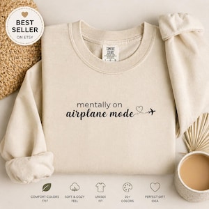 K&ouml;nnte beinhalten: Ein cremefarbenes Sweatshirt mit dem schwarzen Aufdruck "mentally on airplane mode". Ein kleines Herz und ein Flugzeug folgen dem Text. Das Sweatshirt hat einen Rundhalsausschnitt und lange &Auml;rmel. Die Worte "BEST SELLER ON ETSY" stehen in einem Kreis oben links.