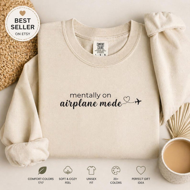 K&ouml;nnte beinhalten: Ein cremefarbenes Sweatshirt mit dem schwarzen Aufdruck "mentally on airplane mode". Ein kleines Herz und ein Flugzeug folgen dem Text. Das Sweatshirt hat einen Rundhalsausschnitt und lange &Auml;rmel. Die Worte "BEST SELLER ON ETSY" stehen in einem Kreis oben links.