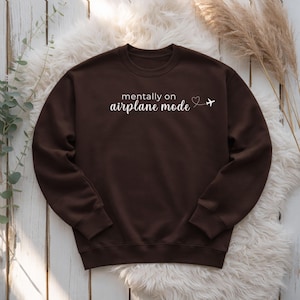 K&ouml;nnte beinhalten: Dunkelbraunes Sweatshirt mit wei&szlig;em Schriftzug "mentally on airplane mode", Herz und Flugzeug-Grafik. Das Sweatshirt mit Rundhalsausschnitt ist aus weichem Material.