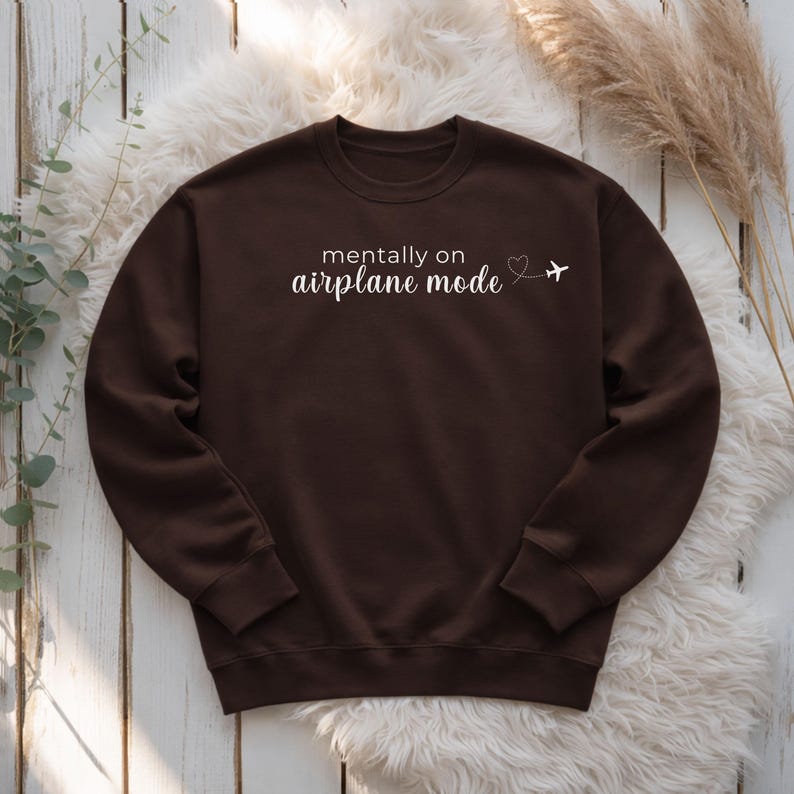 K&ouml;nnte beinhalten: Dunkelbraunes Sweatshirt mit wei&szlig;em Schriftzug "mentally on airplane mode", Herz und Flugzeug-Grafik. Das Sweatshirt mit Rundhalsausschnitt ist aus weichem Material.