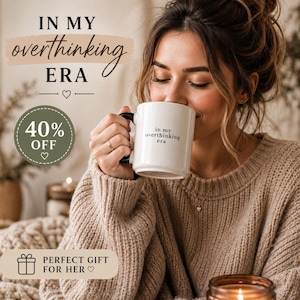 May include: A white ceramic mug with a black handle, featuring the text "in my overthinking era." The image also includes text that says "IN MY overthinking ERA" and "40% OFF". The mug is held by a person wearing a beige sweater.