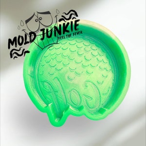 May include: A bright green, circular mold with a textured surface and the word "JUNKIE" in black text. The mold has a scalloped edge and the text "MOLD" and "FEEL THE FEVER" are also visible.