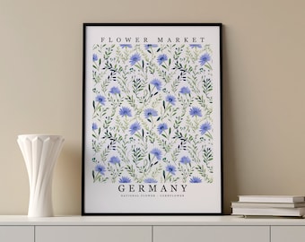 May include: A framed print with a white background and a repeating pattern of blue cornflowers and green leaves. The text "FLOWER MARKET" is at the top and "GERMANY" is at the bottom with the text "NATIONAL FLOWER - CORNFLOWER" below it.
